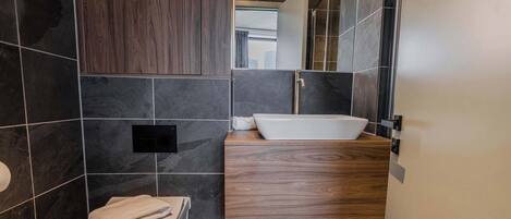 Un baño moderno con inodoro, lavabo sobre encimera y espejo.