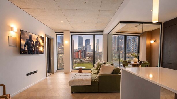 A modern living room with a large window, a green sofa, and a flat-screen TV on the wall.