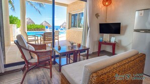 A room with a view of a pool, a TV, and a dining area with chairs and a table. - Newly Renovated Bright and Relaxing Studio (Akumal)