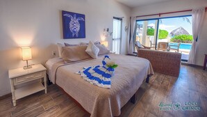 A bedroom with a bed, a nightstand, a lamp, a painting, and a view of the pool outside. - Newly Renovated Bright and Relaxing Studio (Akumal)