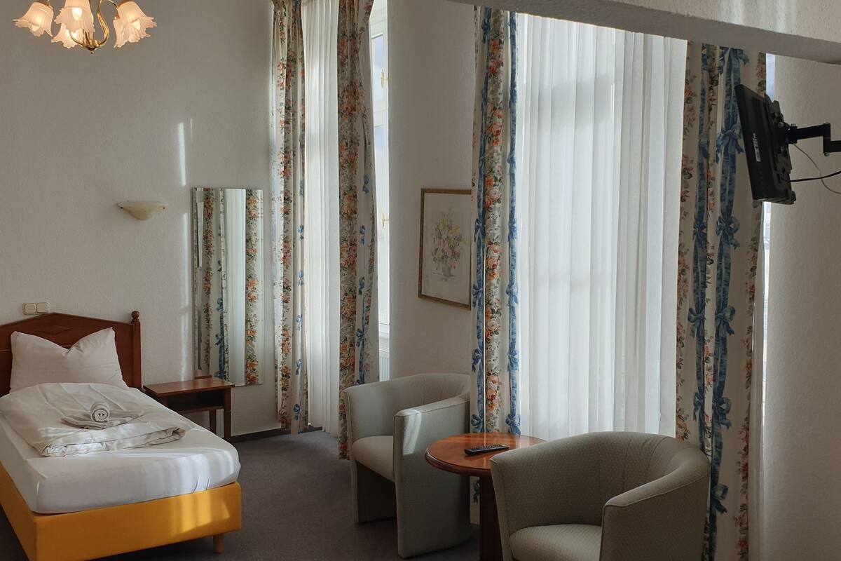 A hotel room with a bed, a chair, a small table, a TV, and curtains.