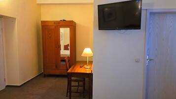 Habitación de hotel con un armario de madera, una mesa con lámpara, un televisor montado en la pared y una puerta.