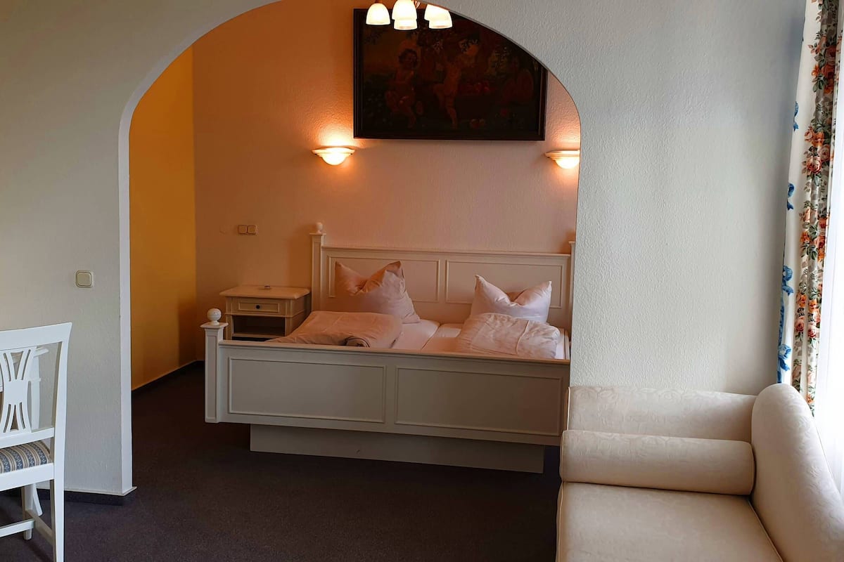 A bedroom with a bed, a chair, a desk, and a painting on the wall.