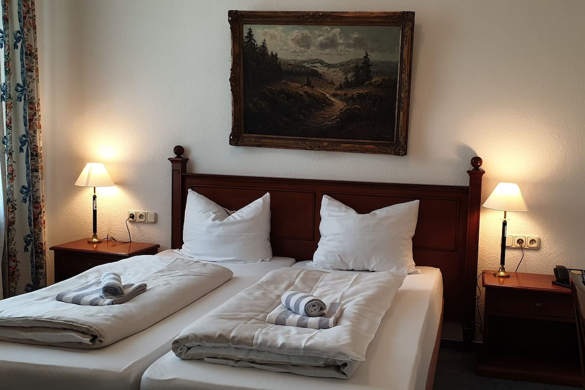 A neatly made double bed with two pillows, a wooden headboard, and two bedside tables with lamps. A painting is hung above the bed.