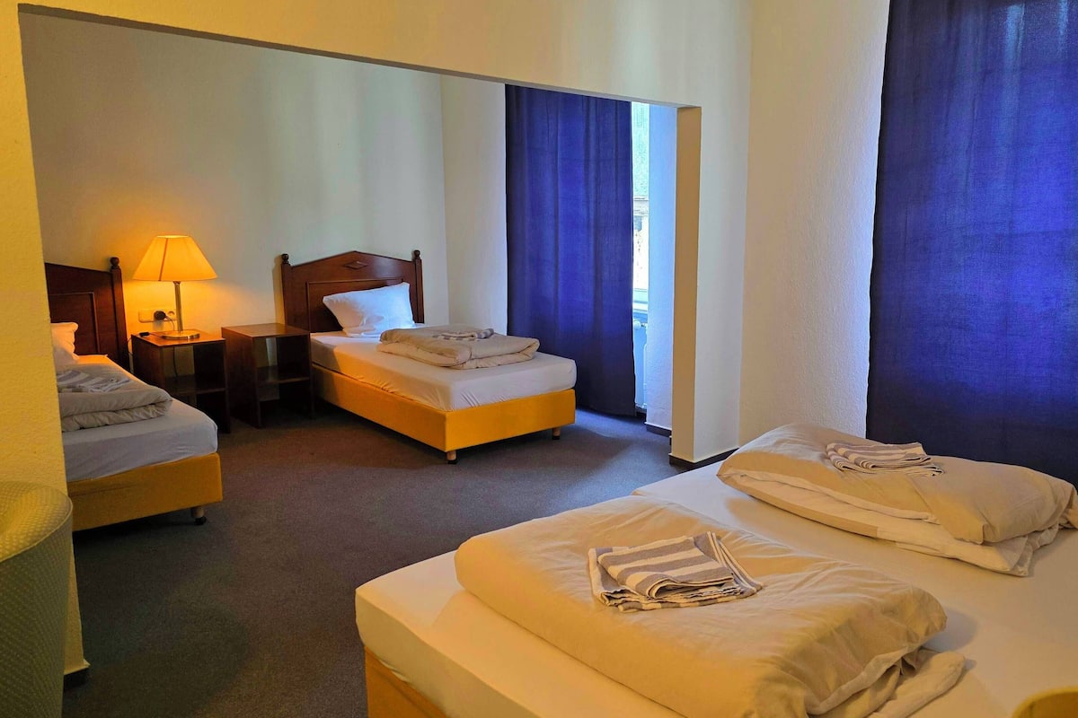 A hotel room with two beds, a desk, a lamp, and a television.