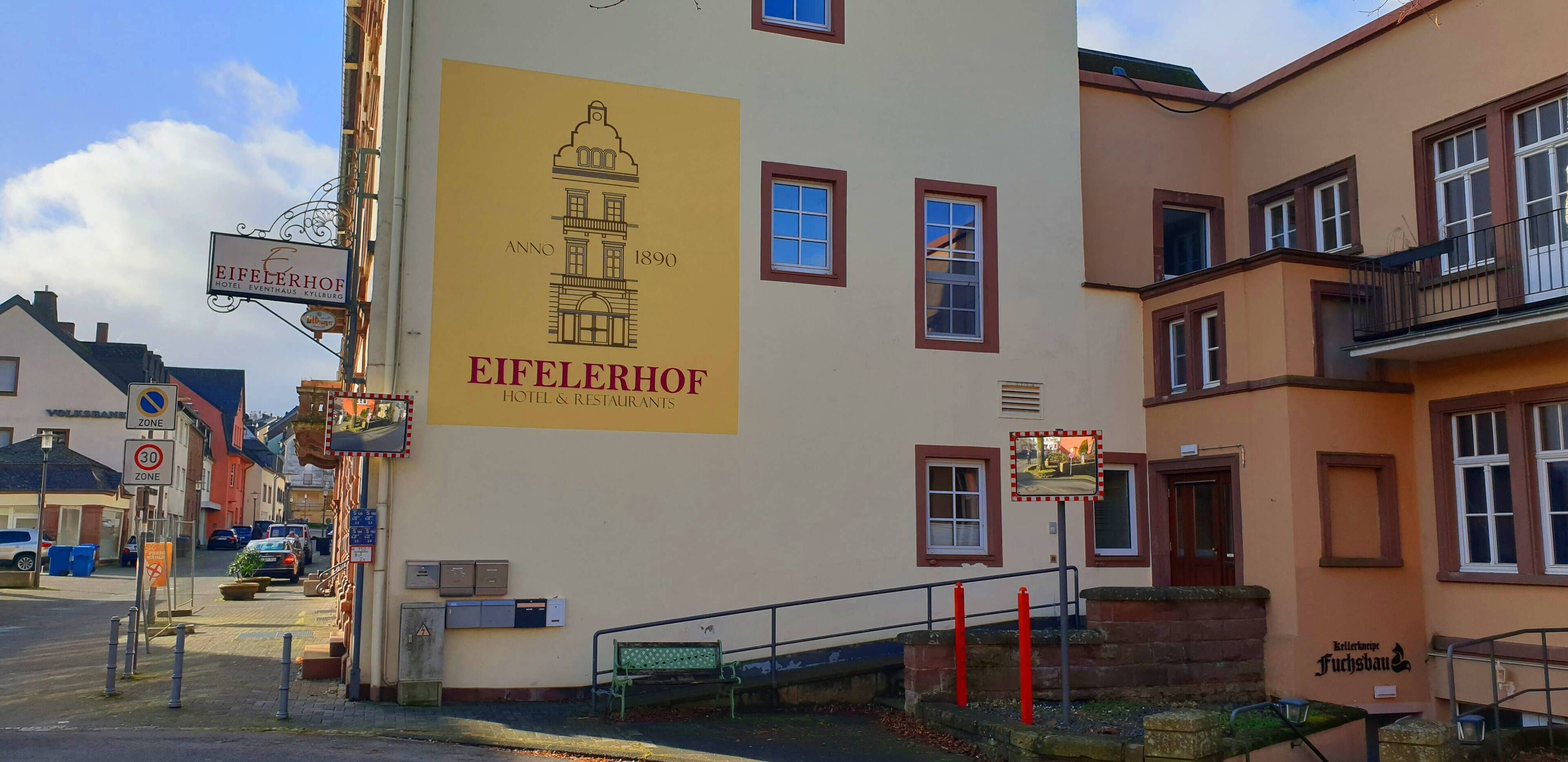 Un bâtiment sur lequel est apposée une grande enseigne pour l’hôtel et les restaurants Eifelerhof, avec une illustration représentant un bâtiment historique.