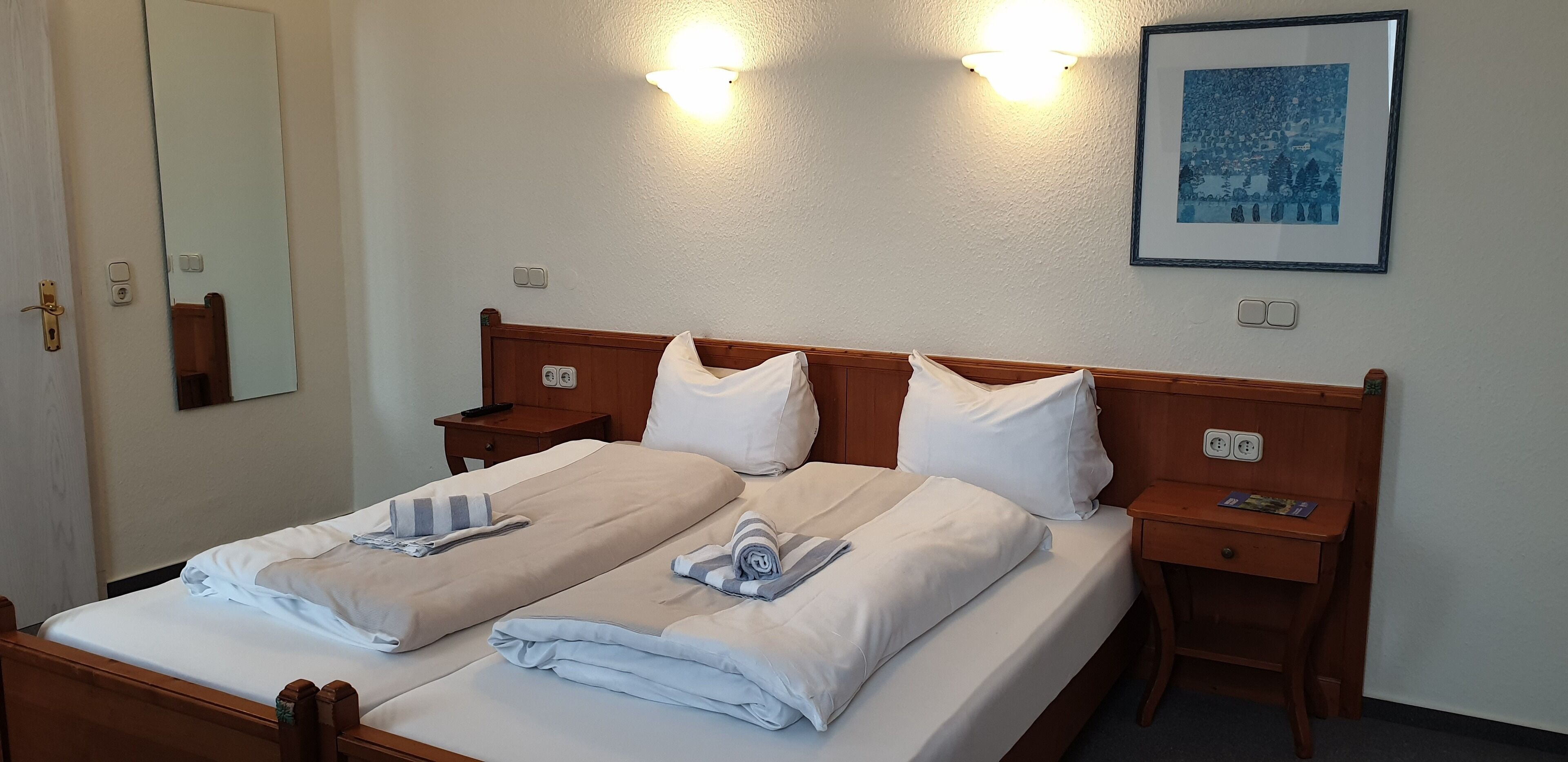 A double bed with two pillows, a wooden headboard, bedside tables, and a framed picture on the wall.