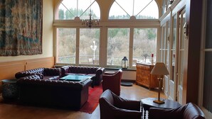 A spacious living room with a large window, leather sofas, a red rug, and a chandelier. - Hotel Eifeler Hof Kyllburg (Kyllburg)