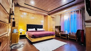 A wooden-paneled room with a bed, a nightstand, a chair, a table, and a window with curtains. - The Bulevar-Kunsil (Lahul)