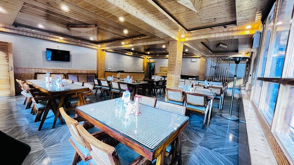 Un restaurant avec des poutres en bois au plafond, plusieurs tables à manger entourées de chaises et un téléviseur à écran plat fixé au mur.