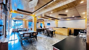 A modern restaurant with wooden interiors, multiple dining tables, and a bar area. - The Bulevar-Kunsil (Lahul)