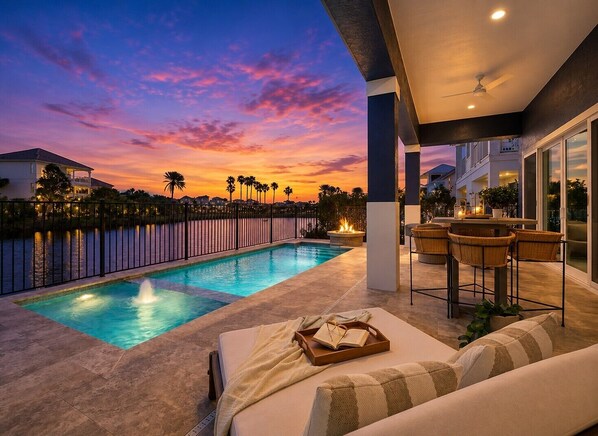 A poolside area with a view of the sunset, a lounge chair, a table with a tray, and a bar area.