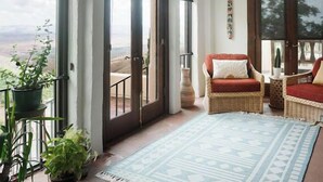 Une pièce spacieuse dotée de grandes portes en arc donnant sur un balcon, d’un canapé en osier, d’un luminaire suspendu et d’un tapis à motifs.