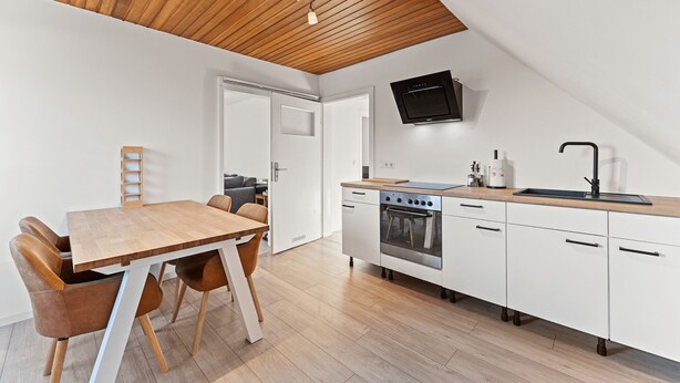 Een moderne keuken met een houten plafond, witte kasten, een inbouwoven en een flatscreen televisie.