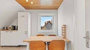 Een moderne keuken met witte kasten, een houten plafond en een eethoek met een tafel en stoelen.