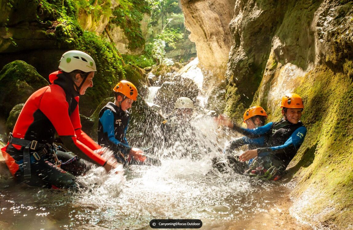 Un grupo de personas con cascos y trajes de neopreno sentadas junto a una cascada en un entorno natural.