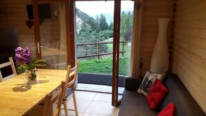 Interior de madera con una mesa de comedor, sillas, un sofá con cojines rojos y vistas a un área boscosa a través de una puerta de cristal.