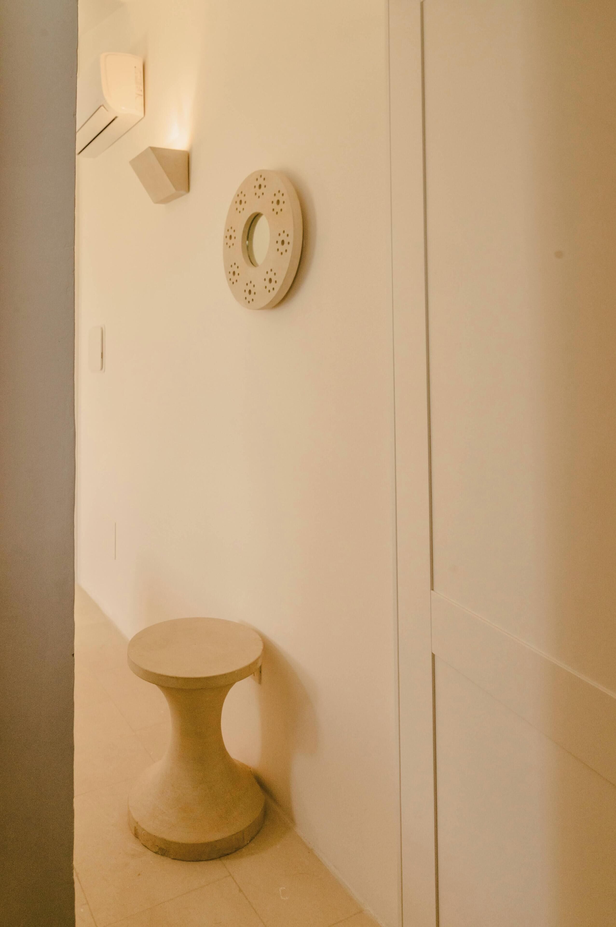 A minimalist bathroom with a round, perforated wall decoration, a small pedestal sink, and a wall-mounted light fixture.