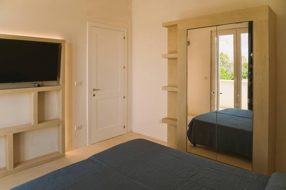 Un dormitorio con cama, televisor montado en la pared, armario y puerta corredera de vidrio.