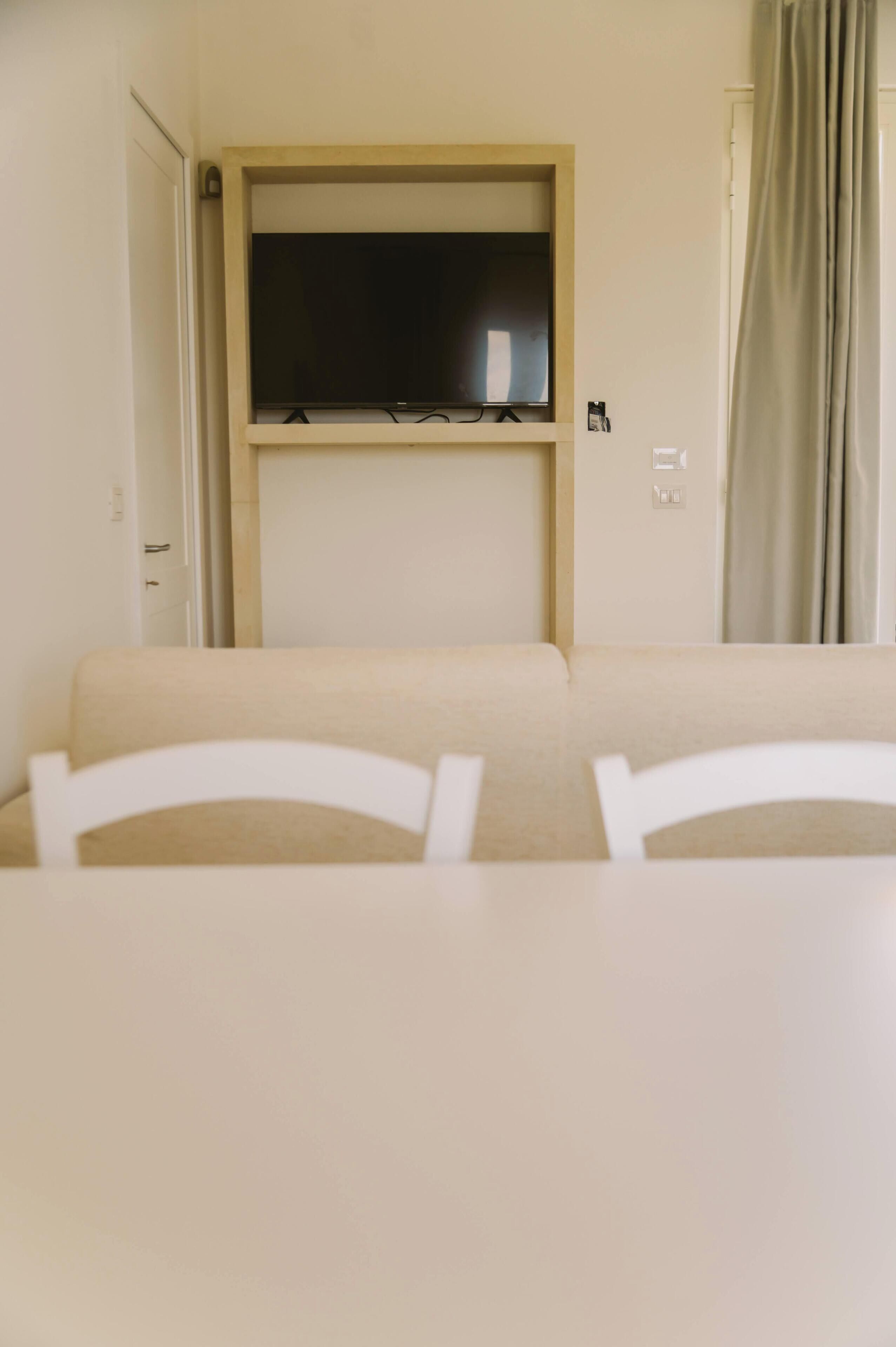 A room with a television mounted on the wall, a sofa, and a table with chairs.