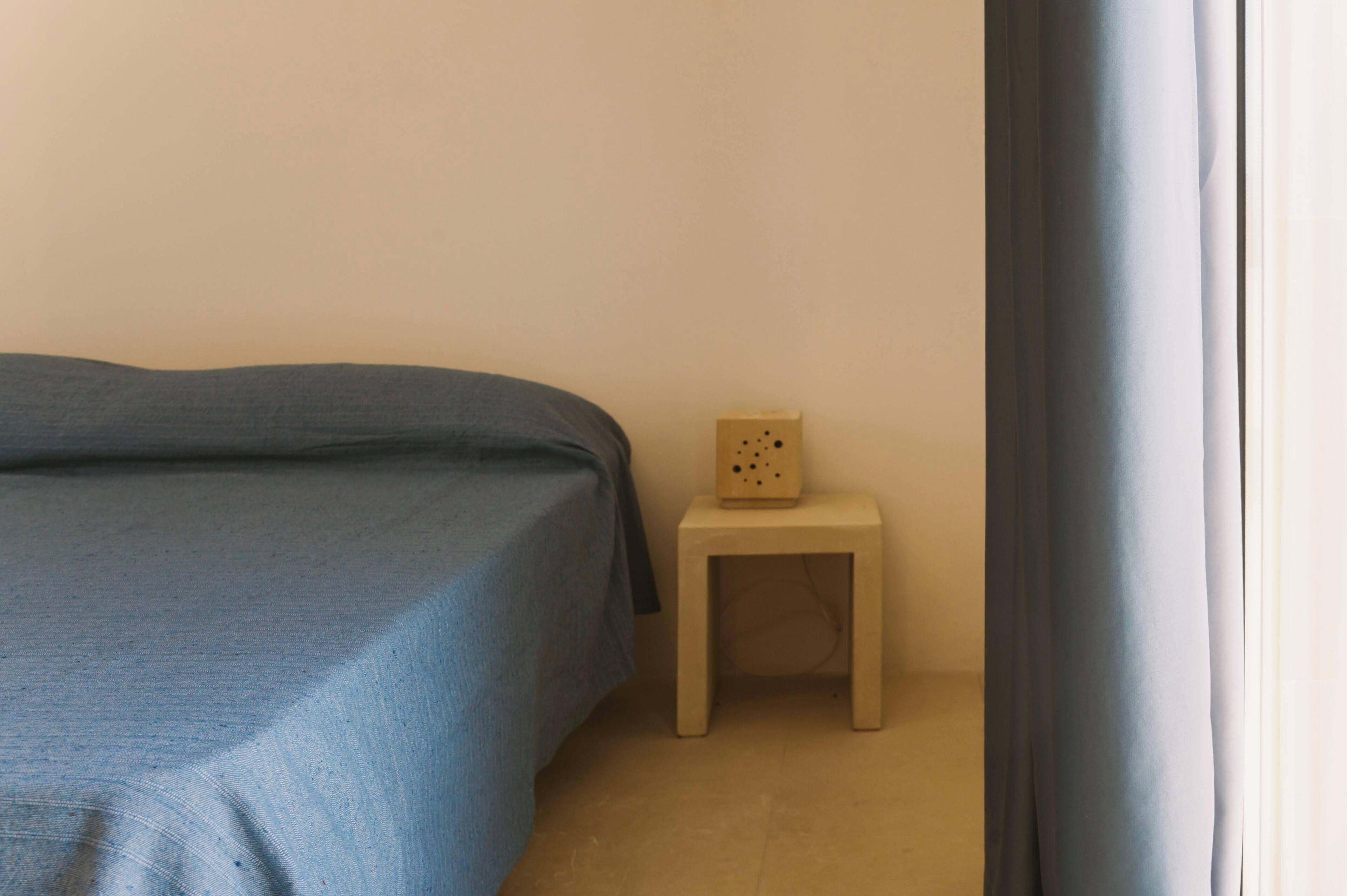 A bedroom with a bed, a small wooden nightstand, and a window with a curtain.