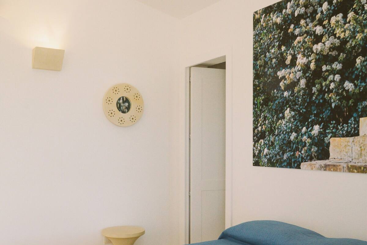 Un dormitorio con una cama, una lámpara de pared, un plato decorativo redondo y una pintura floral.