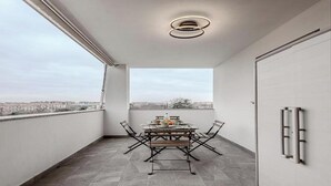 Un balcón con mesa y sillas, vistas de la ciudad y una lámpara moderna.