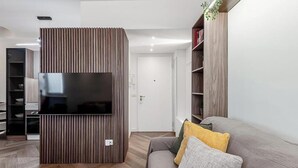 Una sala de estar moderna con un televisor de pantalla plana montado en un panel de madera, un sofá gris con cojines y una estantería.