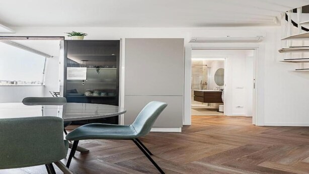 Una cocina moderna con horno empotrado, una zona de comedor con una mesa redonda y dos sillas, y un pasillo que conduce a un baño.