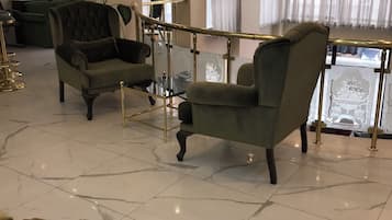 A spacious room with a marble floor, two upholstered armchairs, a glass coffee table, and a view through a glass railing.