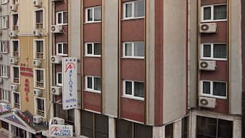Un hotel de varios pisos con unidades de aire acondicionado, un letrero que dice 'Hotel Avlonya', y una vista de la calle con coches estacionados.