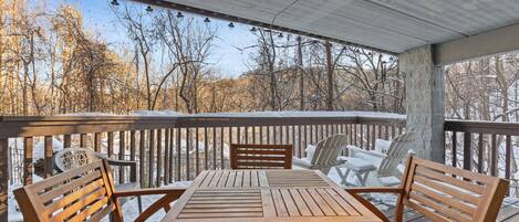 A wooden deck with a table and chairs, surrounded by snow-covered trees.