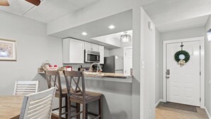 A modern kitchen with white cabinets, a microwave, and a refrigerator. There is a dining area with a wooden table and chairs. - Hilltop Paradise (Gatlinburg)