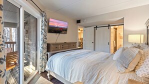 A bedroom with a bed, a TV, a sliding glass door, a wooden bench, and a lamp. - Hilltop Paradise (Gatlinburg)