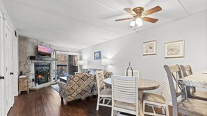 A spacious living room with a fireplace, a ceiling fan, and a dining area with chairs and a table. - Hilltop Paradise (Gatlinburg)