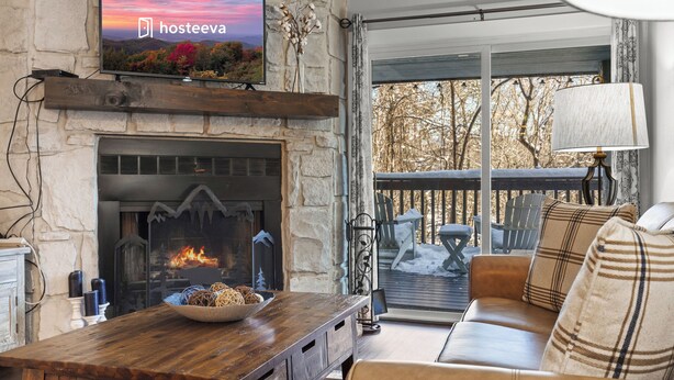 A cozy living room with a stone fireplace, a television mounted above it, and a comfortable seating area with a sofa and cushions. - Hilltop Paradise (Gatlinburg)