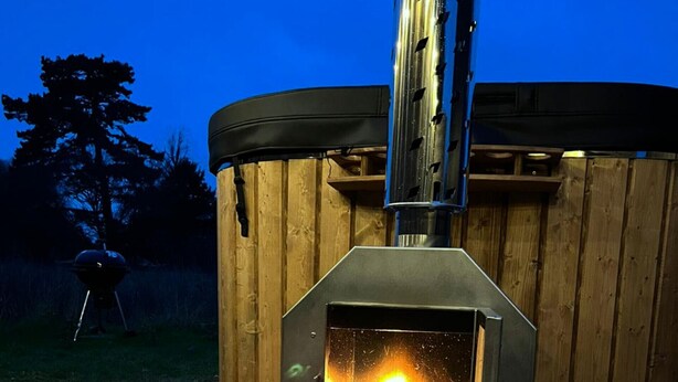A wood-burning stove with a fire burning inside, placed on a concrete patio.