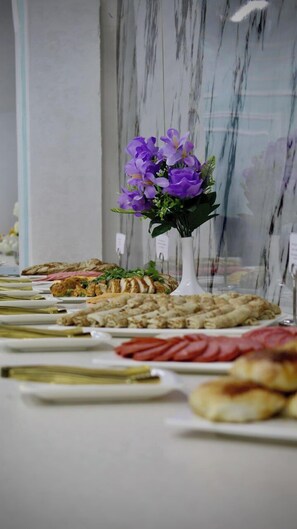 A table with various food items and a vase of purple flowers. - Grand Shosh Hotel (Tashkent)