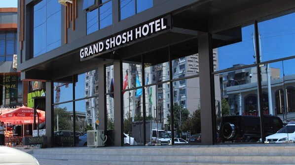 The exterior of the Grand Shosh Hotel with large glass windows reflecting the surrounding buildings and vehicles. - Grand Shosh Hotel (Tashkent)