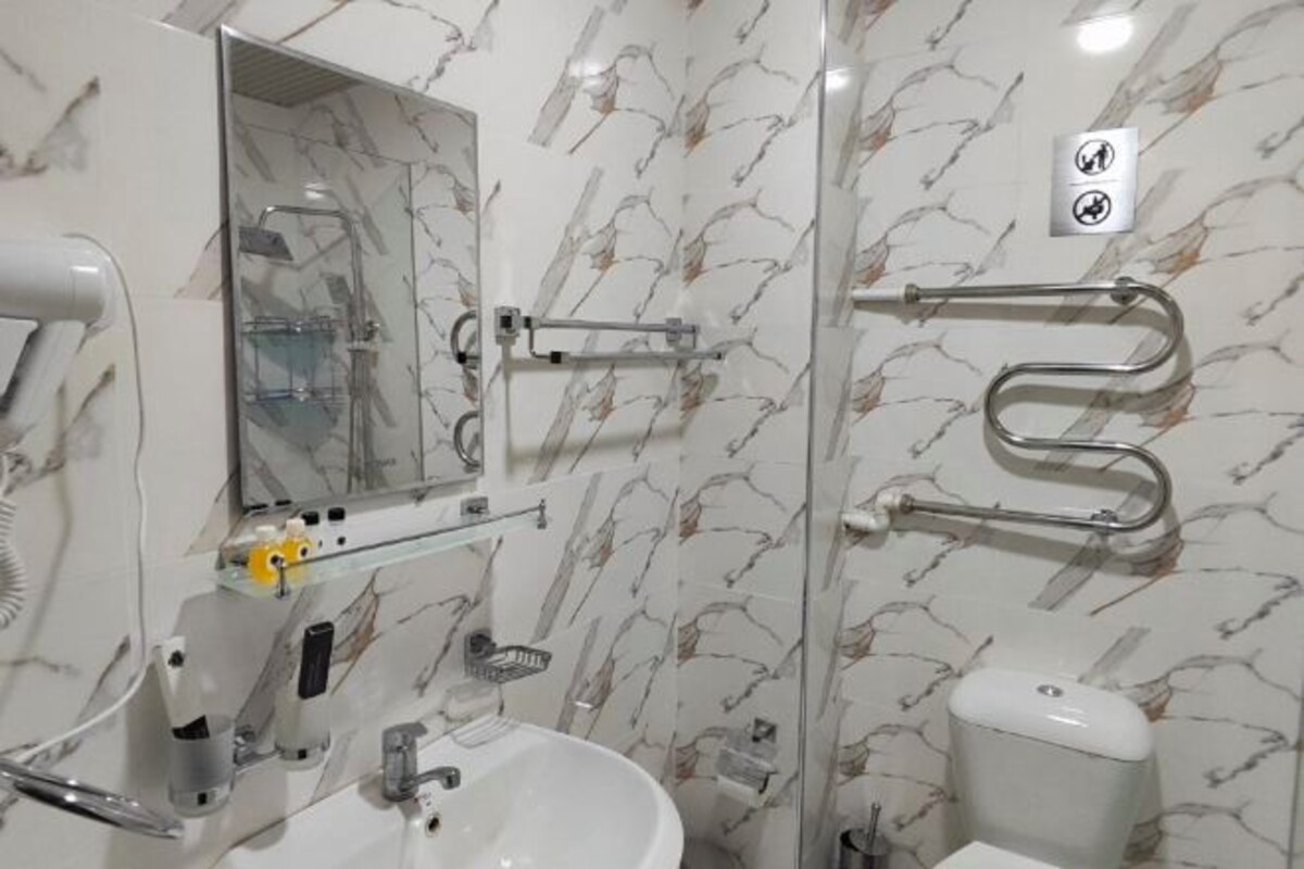 A bathroom with a white sink, mirror, and toilet. There are handrails on the walls and a towel rack.