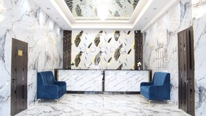 Un área de recepción con paredes y piso de mármol, dos sillones azules y una lámpara moderna.