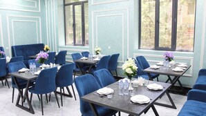 Un comedor con sillas tapizadas en azul y mesas, cada conjunto con platos, vasos y botellas de agua.
