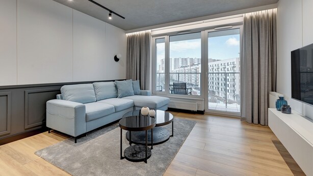 A modern living room with a light blue sofa, a round coffee table, and a large window with curtains. - Seaside Przystań Letnica by Downtown Apartments (Gdansk)