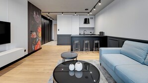A modern living room with a black coffee table, a blue sofa, and a kitchen area with a large island and bar stools. - Seaside Przystań Letnica by Downtown Apartments (Gdansk)