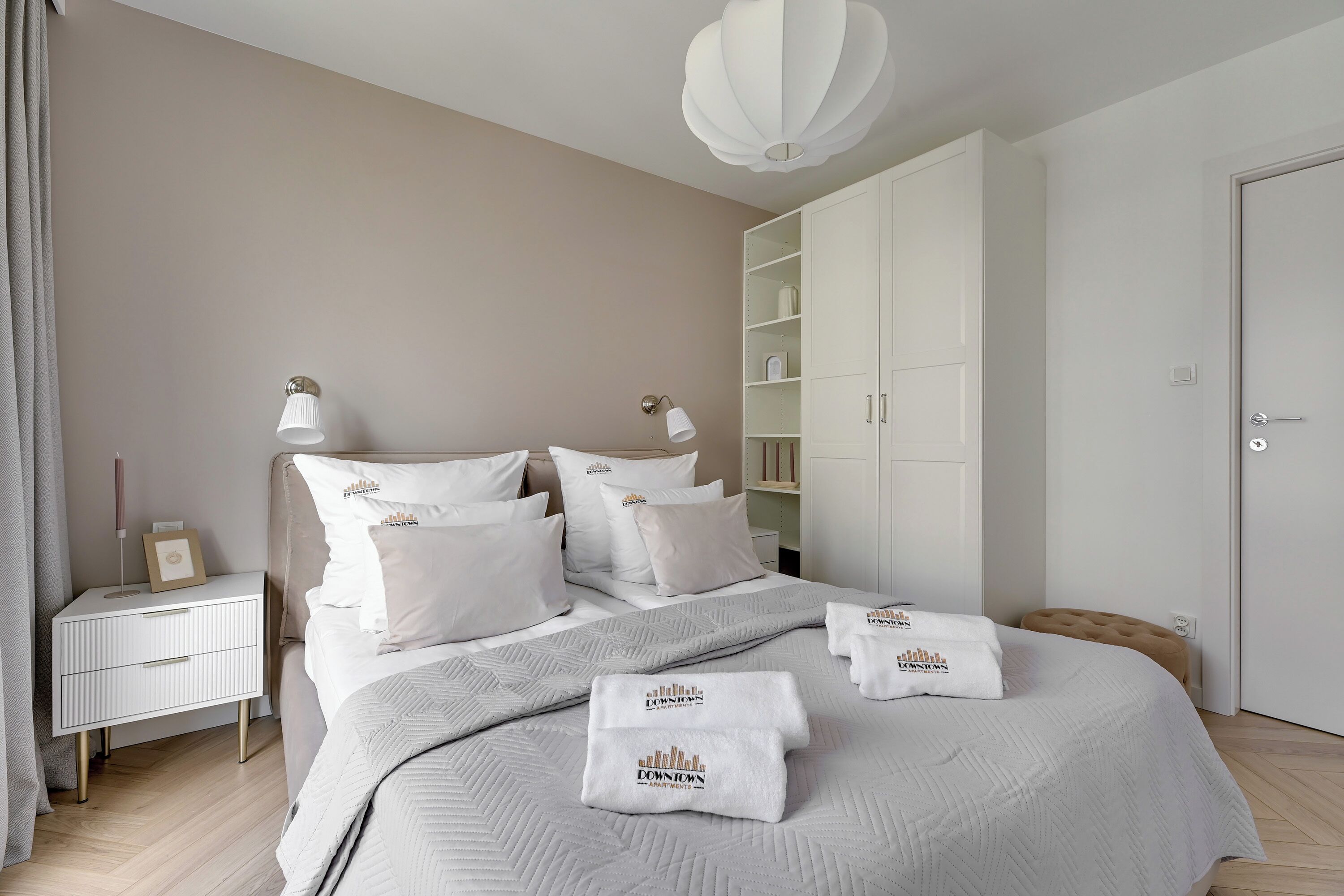 A neatly arranged bedroom with a bed, bedside tables, a wardrobe, and a hanging light fixture.