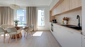 A modern kitchen with a dining area, featuring light wood cabinetry, a black sink, and a dining table with chairs. - Seaside Przystań Letnica by Downtown Apartments (Gdansk)