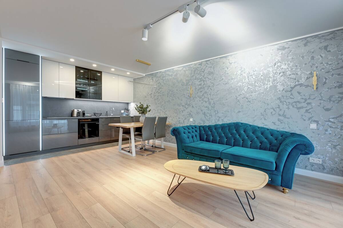 Eine moderne Küche mit Essbereich, einem petrolfarbenen Sofa und einem Couchtisch.