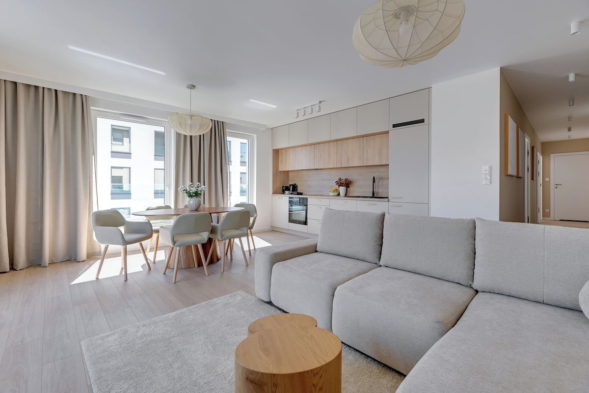 Ein modernes Wohnzimmer mit einer großen, grauen Couch, einem Holztisch und einem Essbereich mit Tisch und Stühlen.