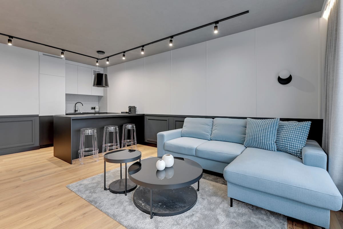 Ein modernes Wohnzimmer mit einem hellblauen Sofa, einem runden Couchtisch und einer Küchenzeile mit Bar.
