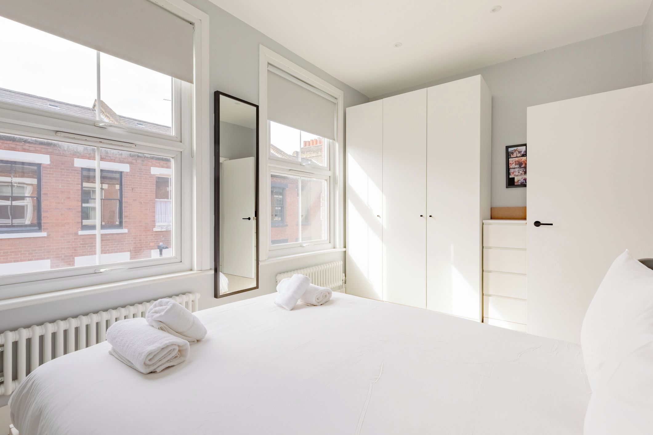 Hotelkamer met een groot bed, een kledingkast, een radiator en een raam met uitzicht op een gebouw van baksteen.